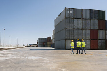 Arbeiter gehen zusammen in der Nähe eines Stapels von Frachtcontainern auf einem Industriegelände - AHSF00196