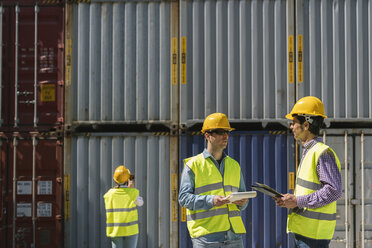 Arbeiter unterhalten sich in der Nähe eines Stapels von Frachtcontainern auf einem Industriegelände - AHSF00197