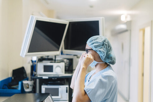 Ärztin, die eine chirurgische Maske bindet und sich auf eine Operation vorbereitet - JCMF00047