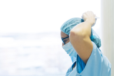 Ärztin, die eine chirurgische Maske bindet und sich auf eine Operation vorbereitet, lizenzfreies Stockfoto