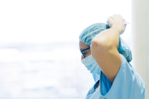 Female doctor tying surgical mask, preparing for surgery - JCMF00049
