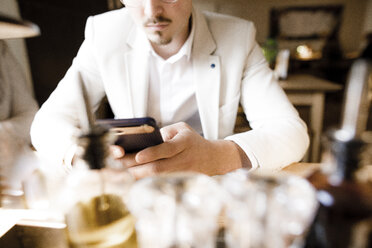 Junger Mann sitzt im Restaurant und benutzt sein Smartphone, Nahaufnahme - KMKF00897