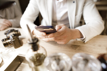 Young man sitting in restaurant, using smartphone, close up - KMKF00898