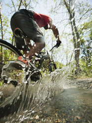 Gemischtrassiger Mann fährt mit dem Mountainbike durch einen Bach - BLEF00139