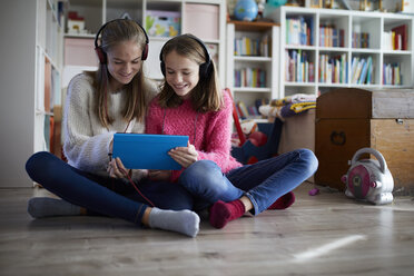 Siblings playing at home with their digital tablets, sitting on ground - RBF07017