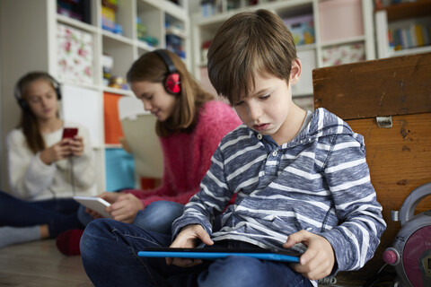 Siblings playing at home with their digital tablets, sitting on ground stock photo