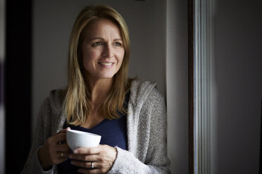 Smiling woman drinking coffee, looking out of window - RBF07030