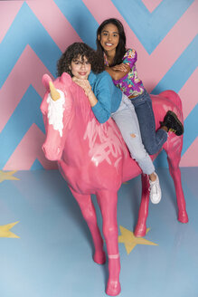Zwei glückliche junge Frauen in einem Indoor-Themenpark mit einer Einhornfigur - AFVF02805