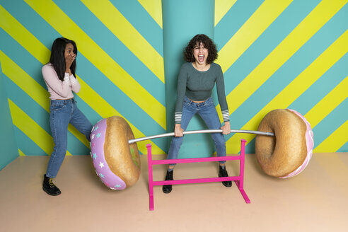 Zwei glückliche junge Frauen in einem Indoor-Vergnügungspark, die sich mit übergroßen Donuts vergnügen - AFVF02814