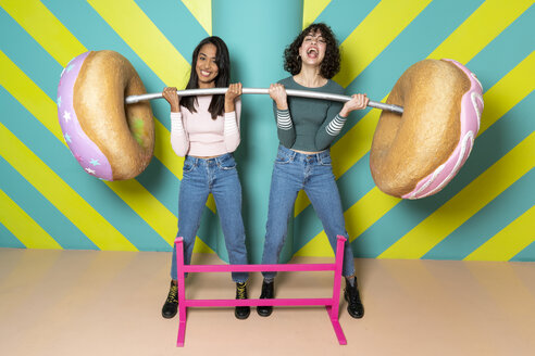 Zwei glückliche junge Frauen in einem Indoor-Vergnügungspark, die sich mit übergroßen Donuts vergnügen - AFVF02815