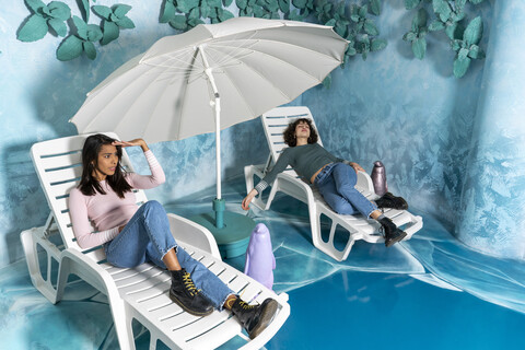 Zwei junge Frauen in einem Indoor-Vergnügungspark liegen auf Liegestühlen an einem künstlichen Meer, lizenzfreies Stockfoto