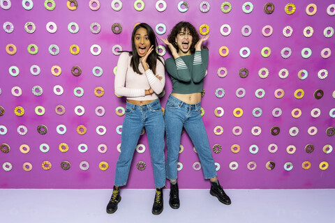 Zwei junge Frauen schreien in einem Indoor-Vergnügungspark mit Donuts an der Wand, lizenzfreies Stockfoto