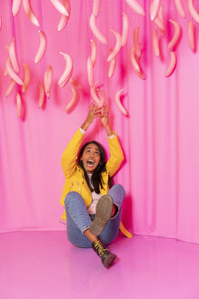 Junge Frau schreit in einem Indoor-Vergnügungspark mit baumelnden rosa Bananen - AFVF02823