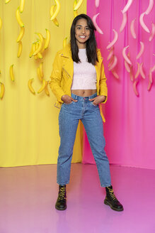 Portrait of a young woman at an indoor theme park with dangling pink and yellow bananas - AFVF02824