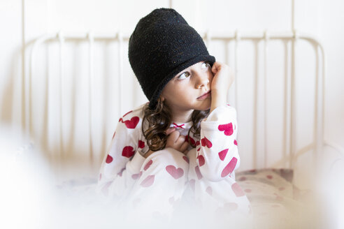 Porträt eines träumenden kleinen Mädchens mit Mütze und Pyjama im Bett sitzend - ERRF01188