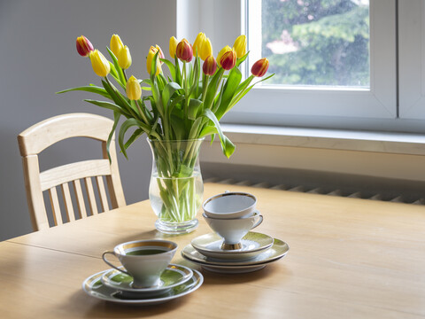 Blumenstrauß aus roten und gelben Tulpen auf einem Esstisch mit Kaffeetassen, lizenzfreies Stockfoto