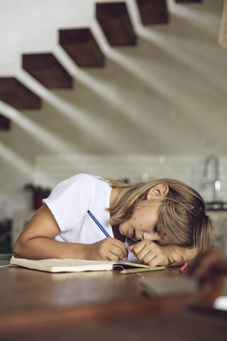 Mädchen sitzt am Tisch und schreibt in ihr Tagebuch, lizenzfreies Stockfoto