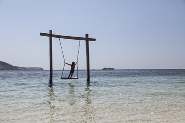 Indonesien, Komodo-Nationalpark, Mädchen auf einer Schaukel im Meer - MCF00148