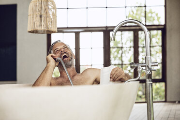Lachender Mann in der Badewanne, der den Duschkopf als Telefonhörer benutzt - MCF00160