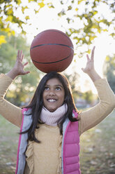 Portrait cute girl balancing basketball on head in autumn park - CAIF23204