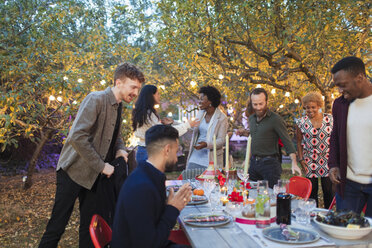 Ankommende Freunde, die zum Abendessen im Garten sitzen - CAIF23242