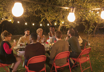 Freunde genießen das Abendessen Gartenparty unter Bäumen mit Lichterketten - CAIF23261