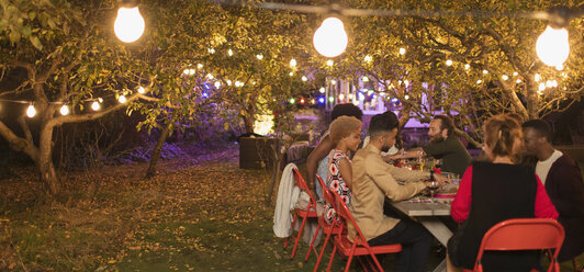 Freunde genießen das Abendessen Gartenparty unter Bäumen mit Lichterketten - CAIF23263