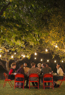 Freunde genießen das Abendessen Gartenparty unter Bäumen mit Lichterketten - CAIF23264