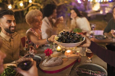 Friends passing mussels, enjoying dinner garden party - CAIF23269