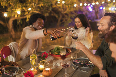 Friends pouring and drinking wine, enjoying dinner garden party - CAIF23275