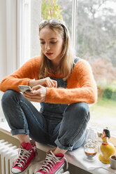 Junge Frau schreibt eine SMS mit einem Smartphone im Fenster - CAIF23311