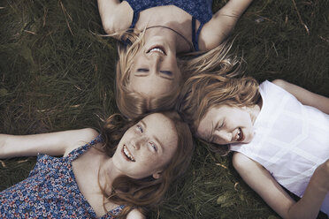 Portrait happy sisters laying in grass - CAIF23316