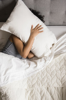 Afroamerikanische Frau liegt auf dem Bett und versteckt ihr Gesicht unter dem Kopfkissen - BLEF00189