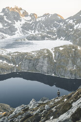 Kaukasischer Mann sitzt auf einem Felsen und bewundert die malerische Aussicht auf einen Bergsee - BLEF00201