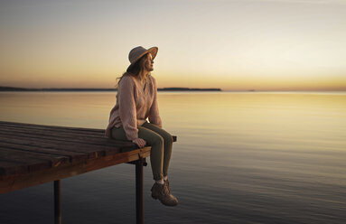 Caucasian woman sitting on dock of lake admiring sunset - BLEF00206