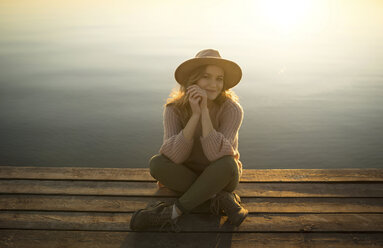 Smiling Caucasian woman sitting on dock of lake - BLEF00208