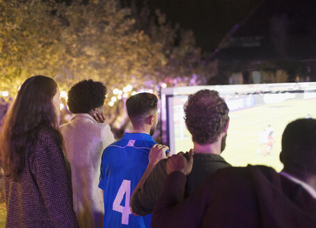 Freunde sehen sich ein Fußballspiel auf einer Projektionsfläche im Hinterhof an - CAIF23353