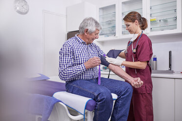 Eine Krankenschwester prüft den Blutdruck eines älteren männlichen Patienten im Untersuchungsraum einer Klinik - CAIF23364