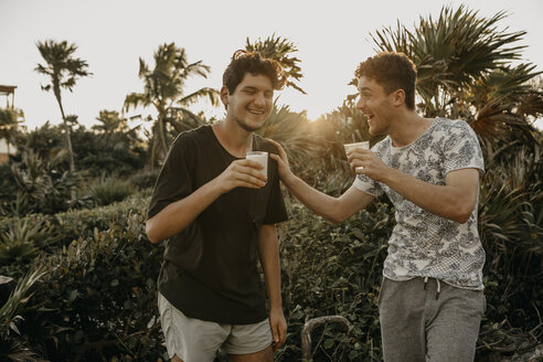 Mexiko, Quintana Roo, Tulum, zwei glückliche junge Männer bei einem Drink im Freien - LHPF00660