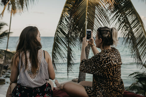 Mexiko, Quintana Roo, Tulum, zwei junge Frauen mit Handy entspannen am Strand - LHPF00664