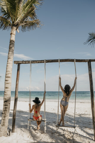 Mexiko, Quintana Roo, Tulum, zwei junge Frauen auf einer Schaukel am Strand, lizenzfreies Stockfoto