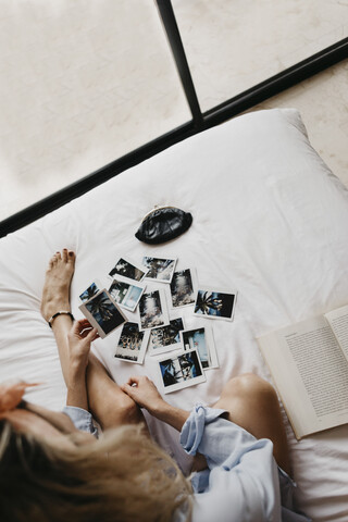 Junge Frau im Bett mit Buch und Polaroidbildern, lizenzfreies Stockfoto