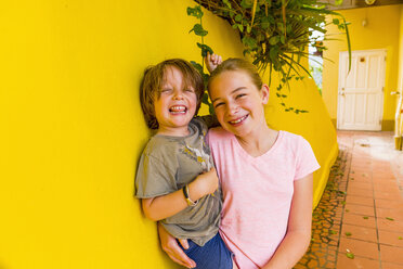 Caucasian girl leaning on yellow wall holding brother - BLEF00231