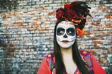 Hispanische Frau in der Nähe einer Backsteinmauer mit Totenkopf-Gesichtsbemalung - BLEF00240