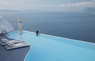 Kaukasische Frau im Infinity-Pool bewundert malerischen Blick auf das Meer - BLEF00242