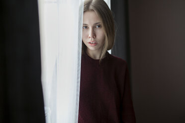 Serious Caucasian woman standing near curtain at window - BLEF00264