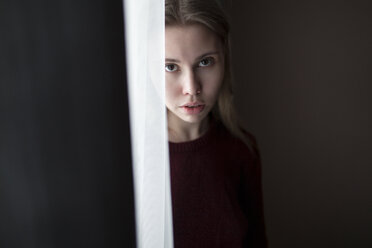 Serious Caucasian woman standing near curtain at window - BLEF00265