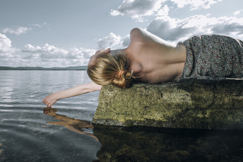 Oben ohne kaukasisches Teenager-Mädchen liegt auf einem Felsen im Meer, lizenzfreies Stockfoto