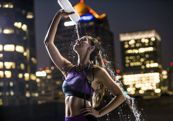 Caucasian woman spraying water on face in city at night - BLEF00288