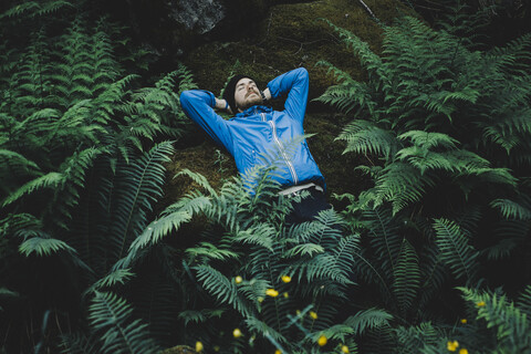 Kaukasischer Mann liegt auf einem Felsen im Laub, lizenzfreies Stockfoto